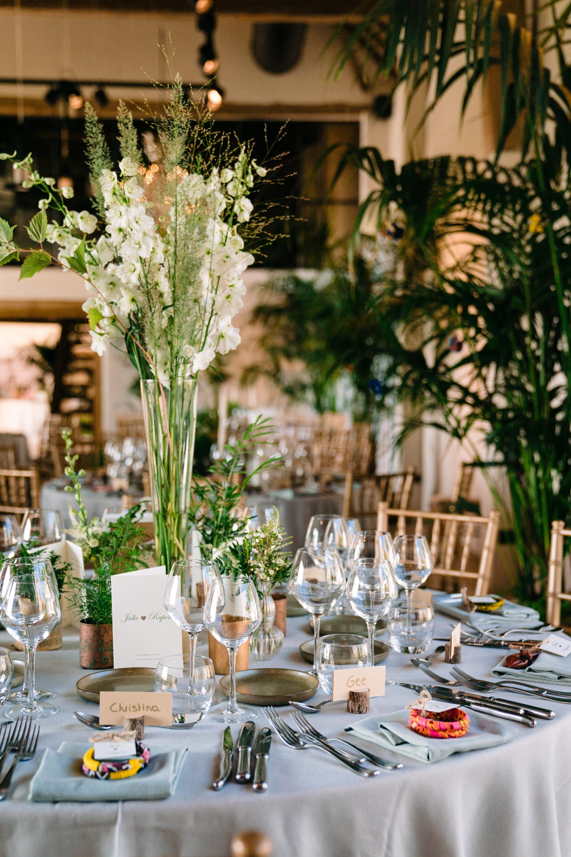 tall vase with white flowers and greens on a table